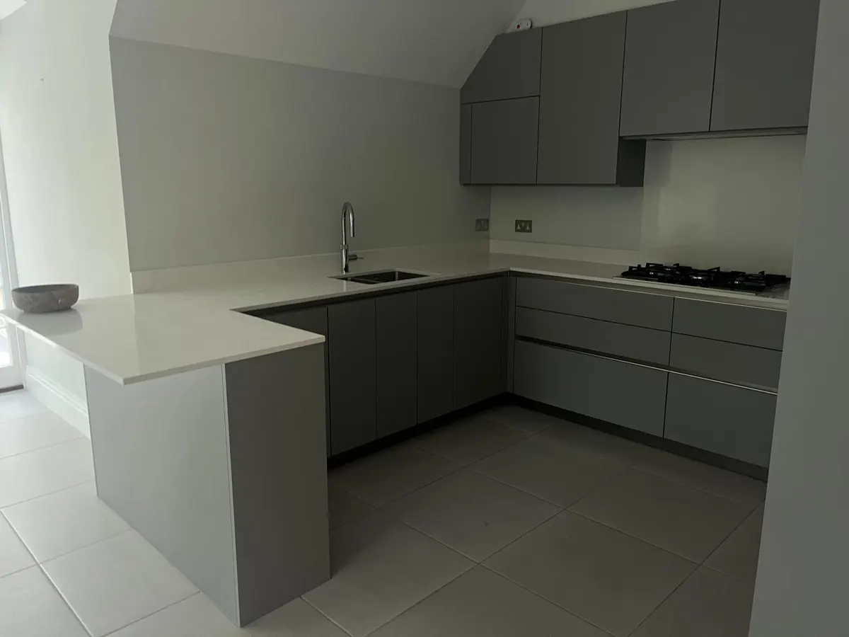 Clean grey U-shaped kitchen with white worktops and tiled floor