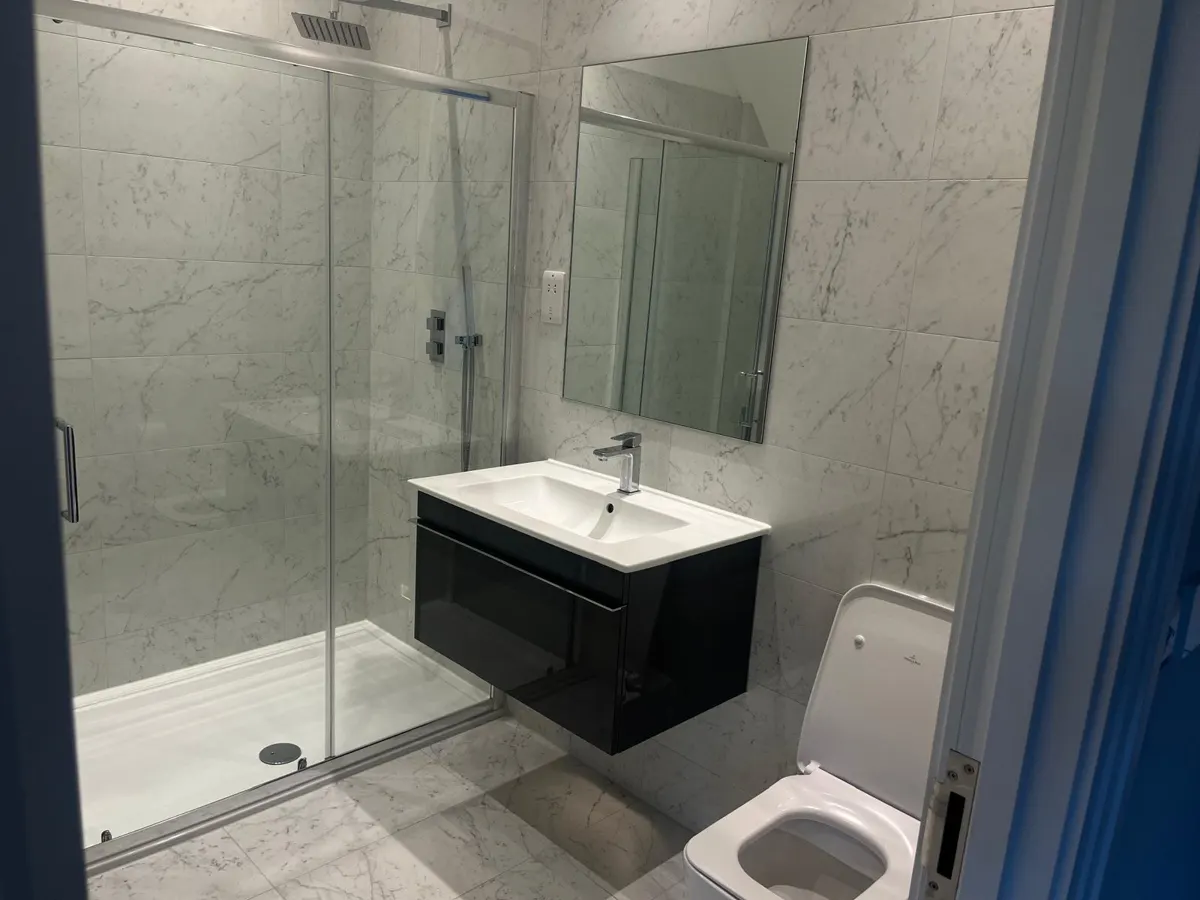 Clean marble-tiled bathroom with glass shower, black vanity unit and mirror